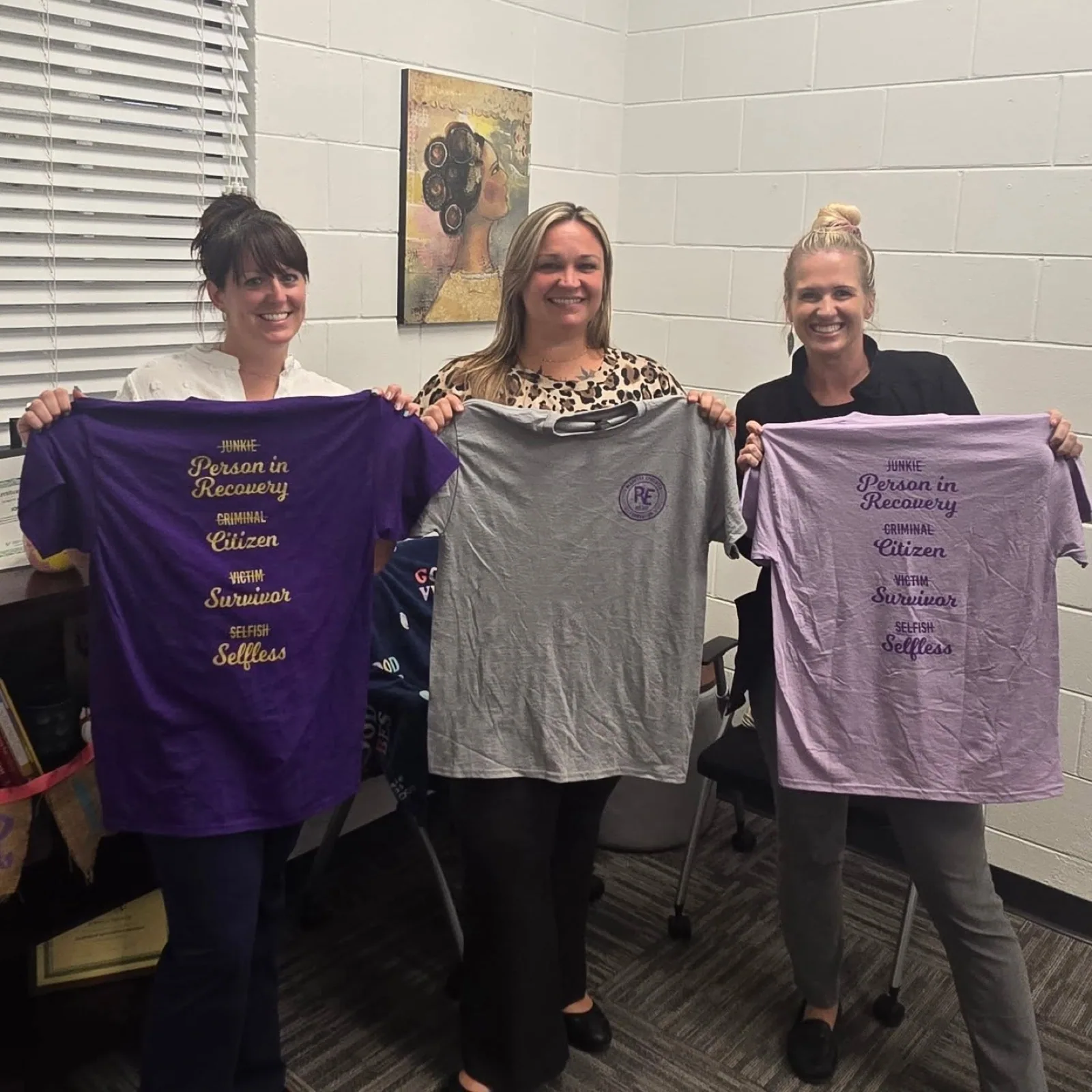 Three people holding up the Recovery Epicenter Foundation t-shirts in purple, ash and lavender